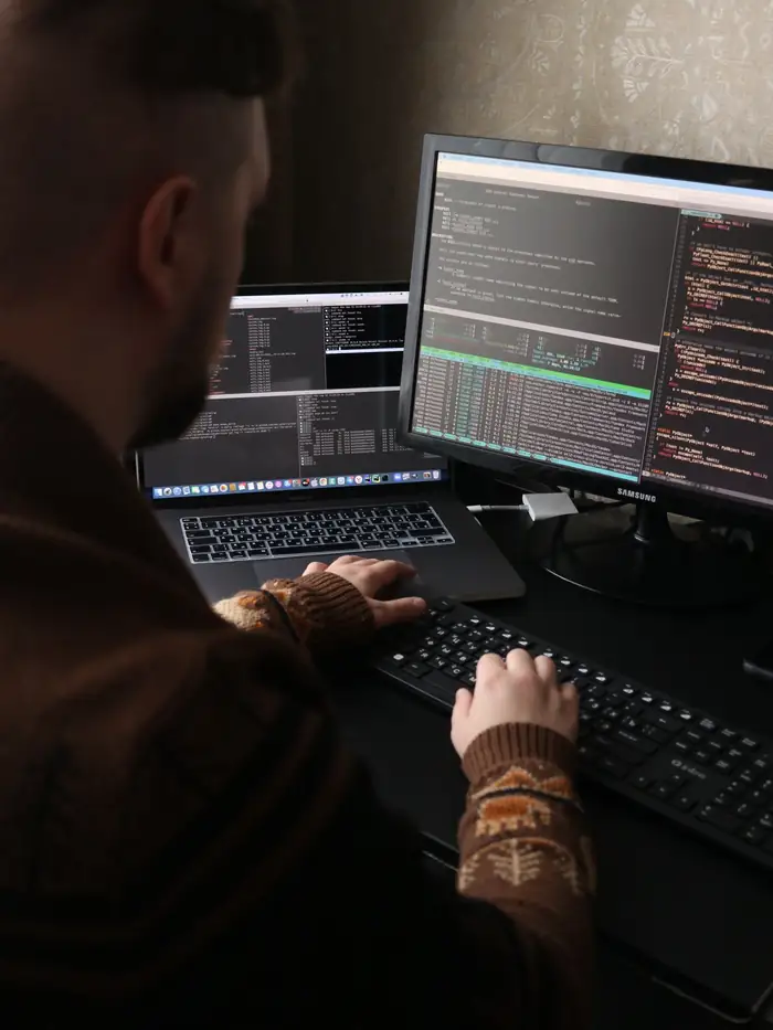 An engineer writes code across two monitors in a dark room