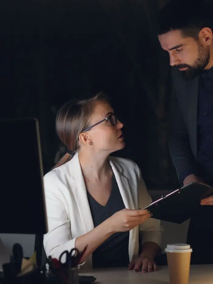 Two leaders review a plan on a tablet in a dimly lit office